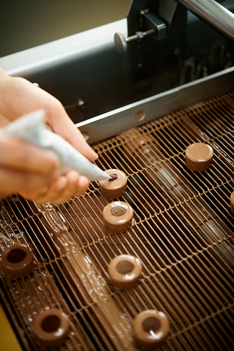 Eine Praline wird mit einem Spritzbeutel mit Schokolade verziert